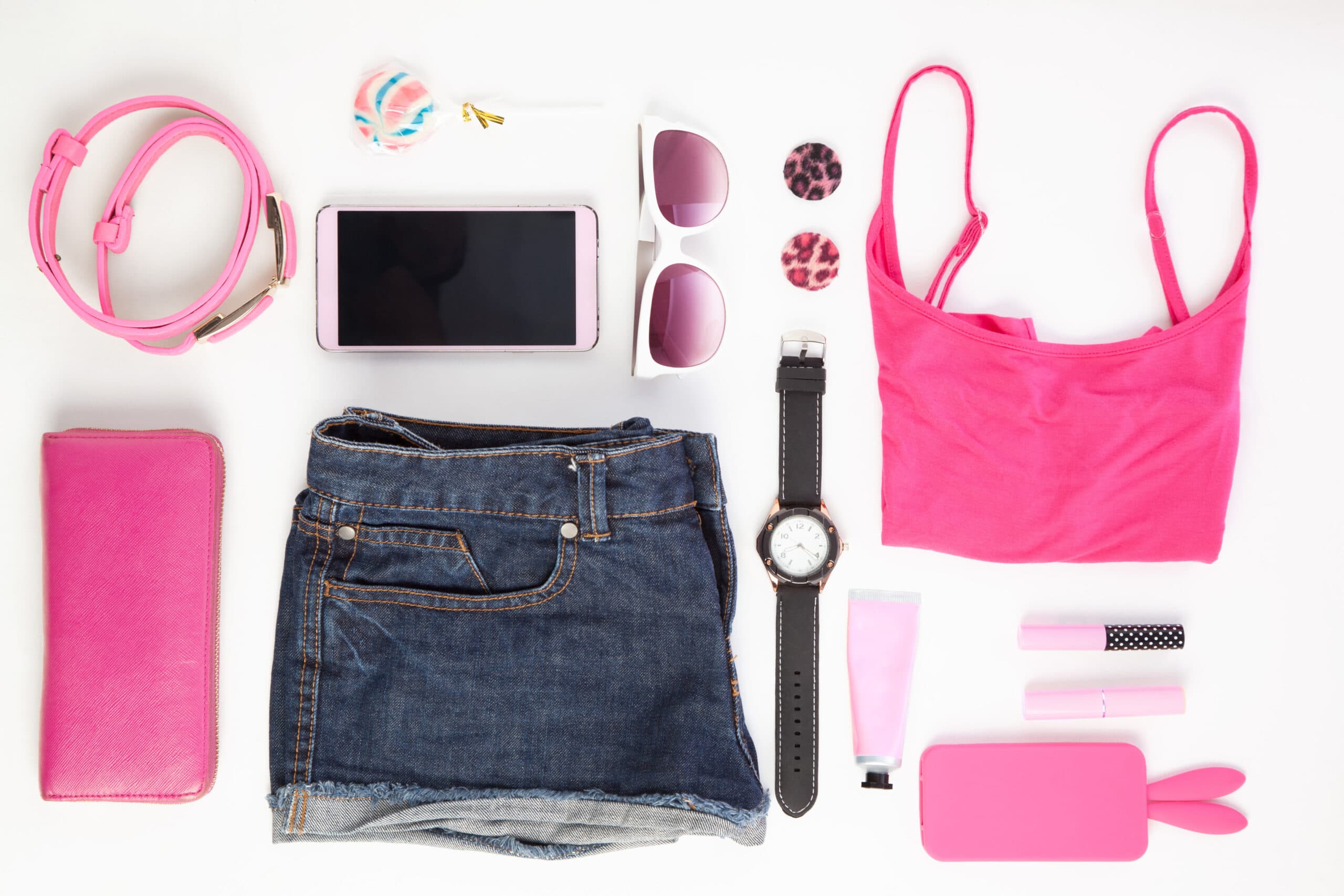 Pink fashion accessories, sunglasses and a smartphone laid out on white